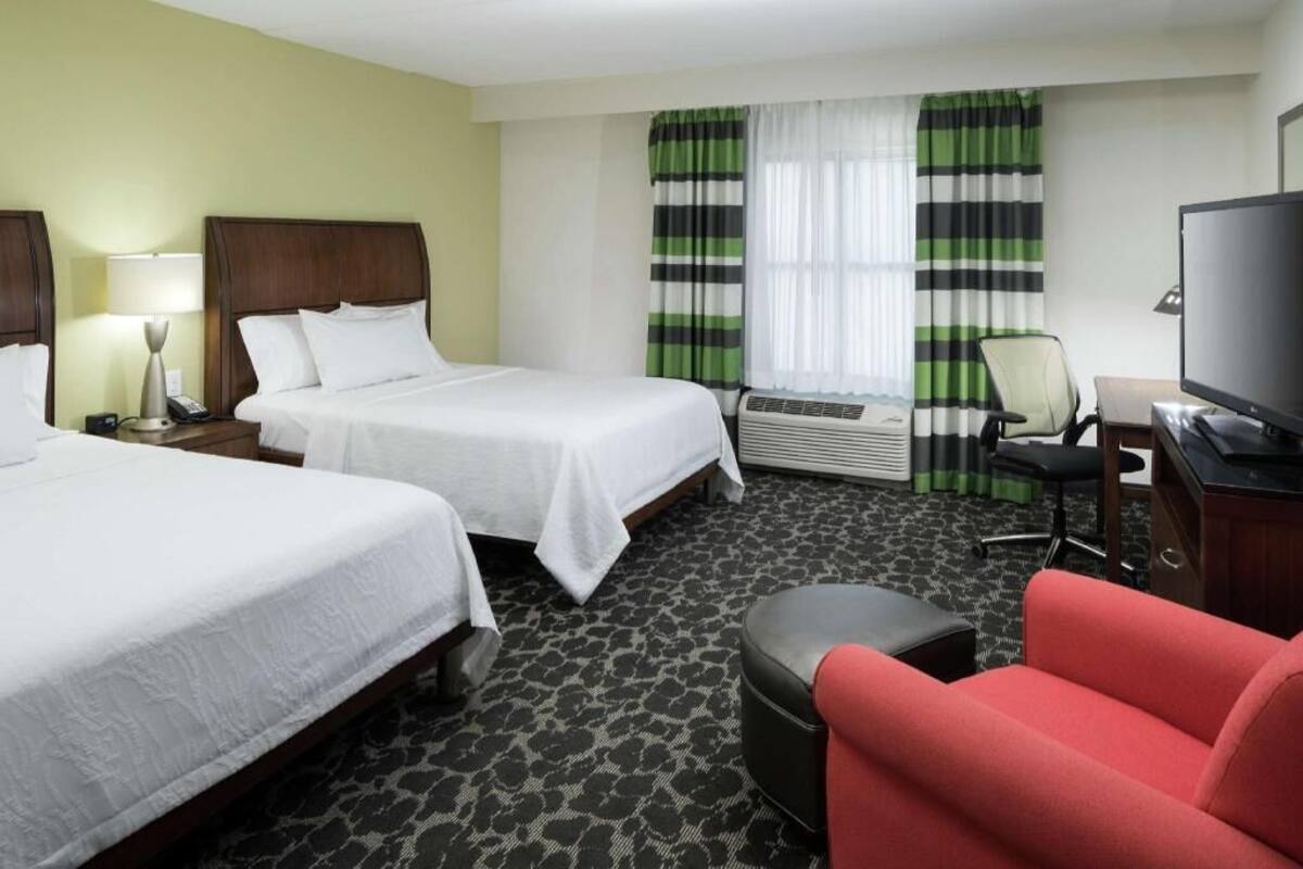 A hotel room with two beds, a desk with a chair, a television, and a red armchair.