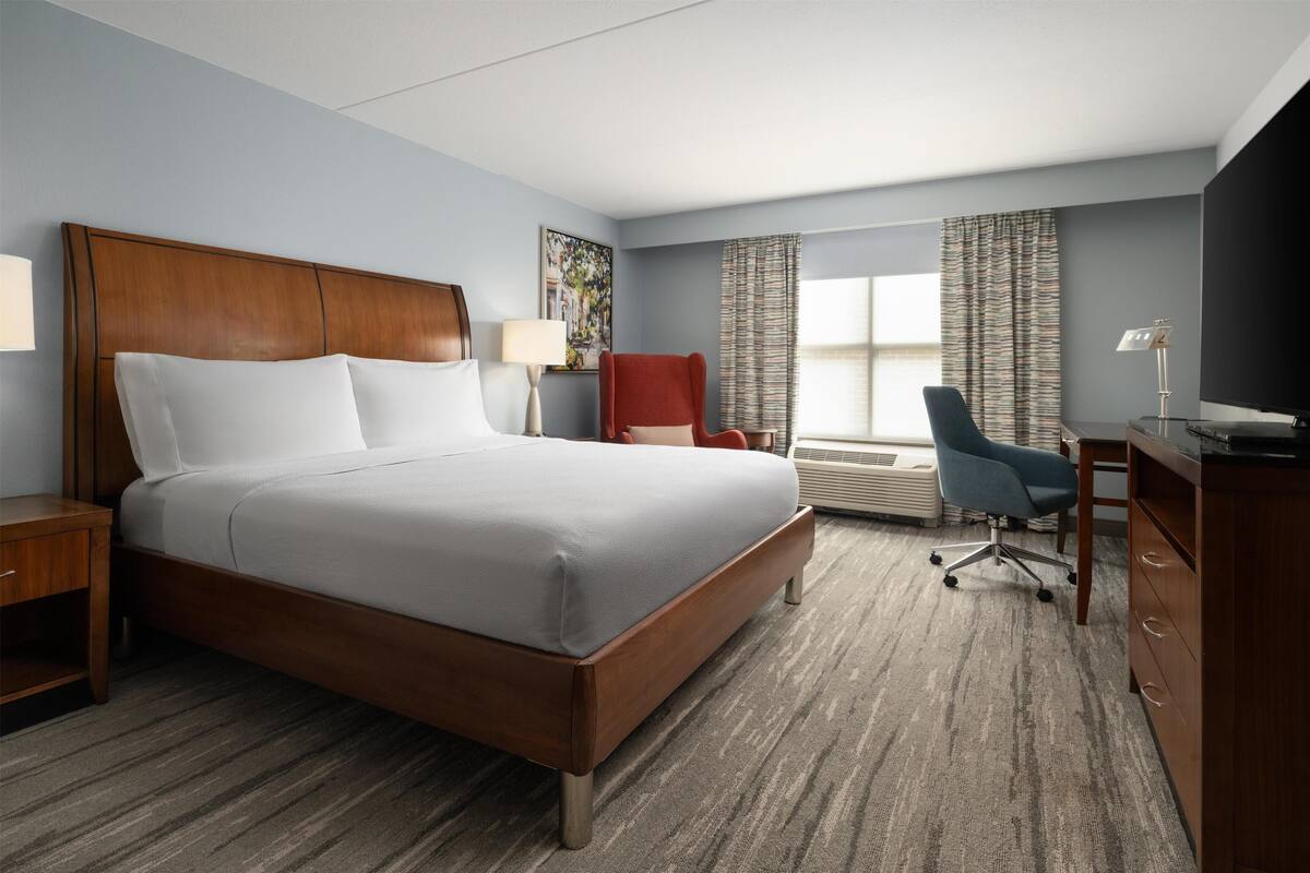 A hotel room with a large bed, a desk, a chair, and a window with curtains.