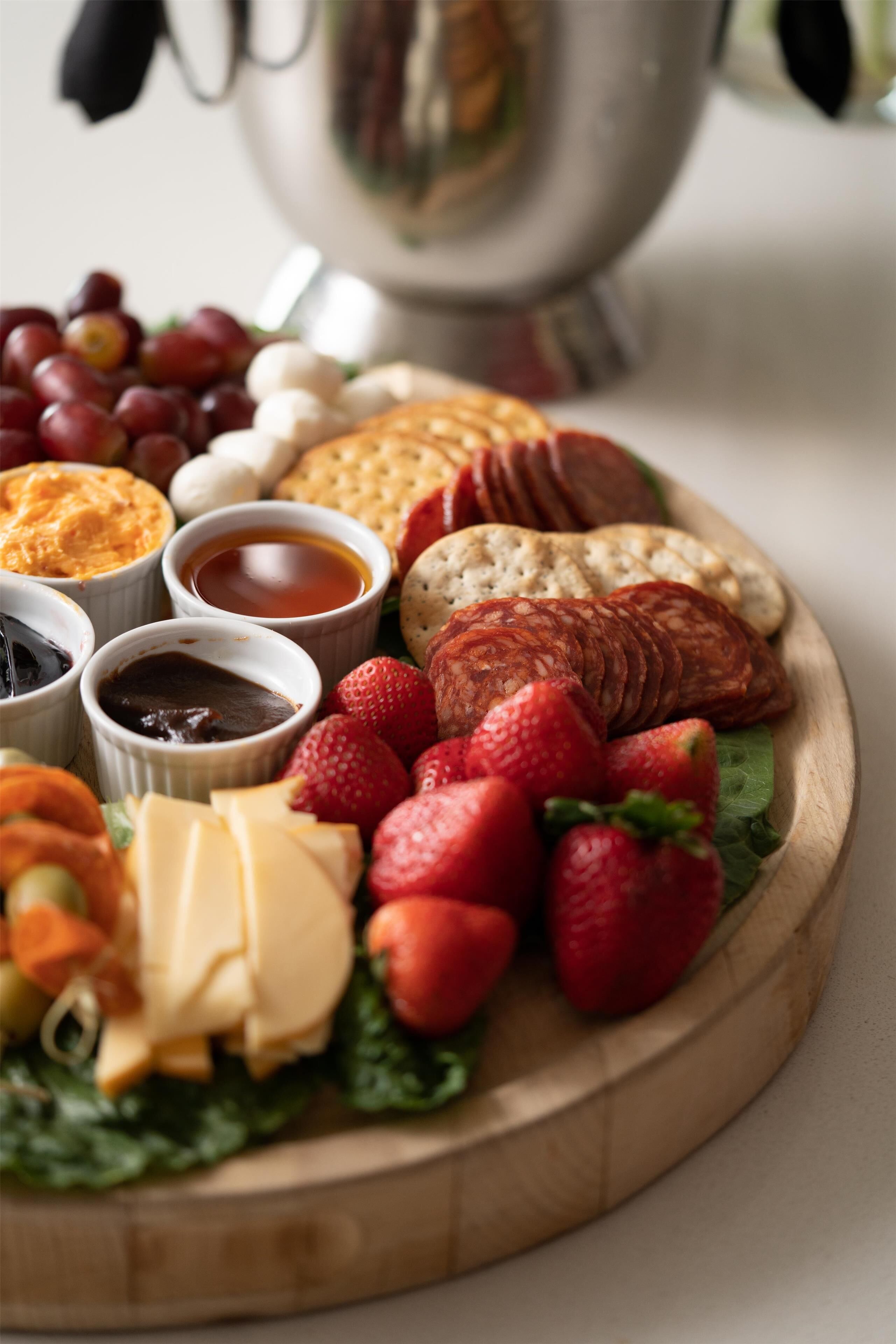A wooden board with various cheeses, strawberries, and crackers.