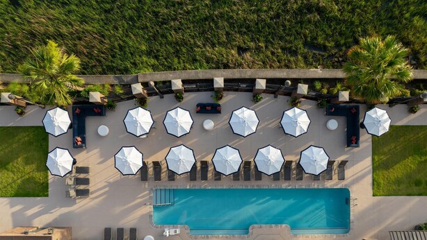 An aerial view of a rooftop pool area with multiple lounge chairs and umbrellas, surrounded by greenery and a swimming pool. - Hilton Garden Inn Charleston Waterfront/Downtown (Charleston)