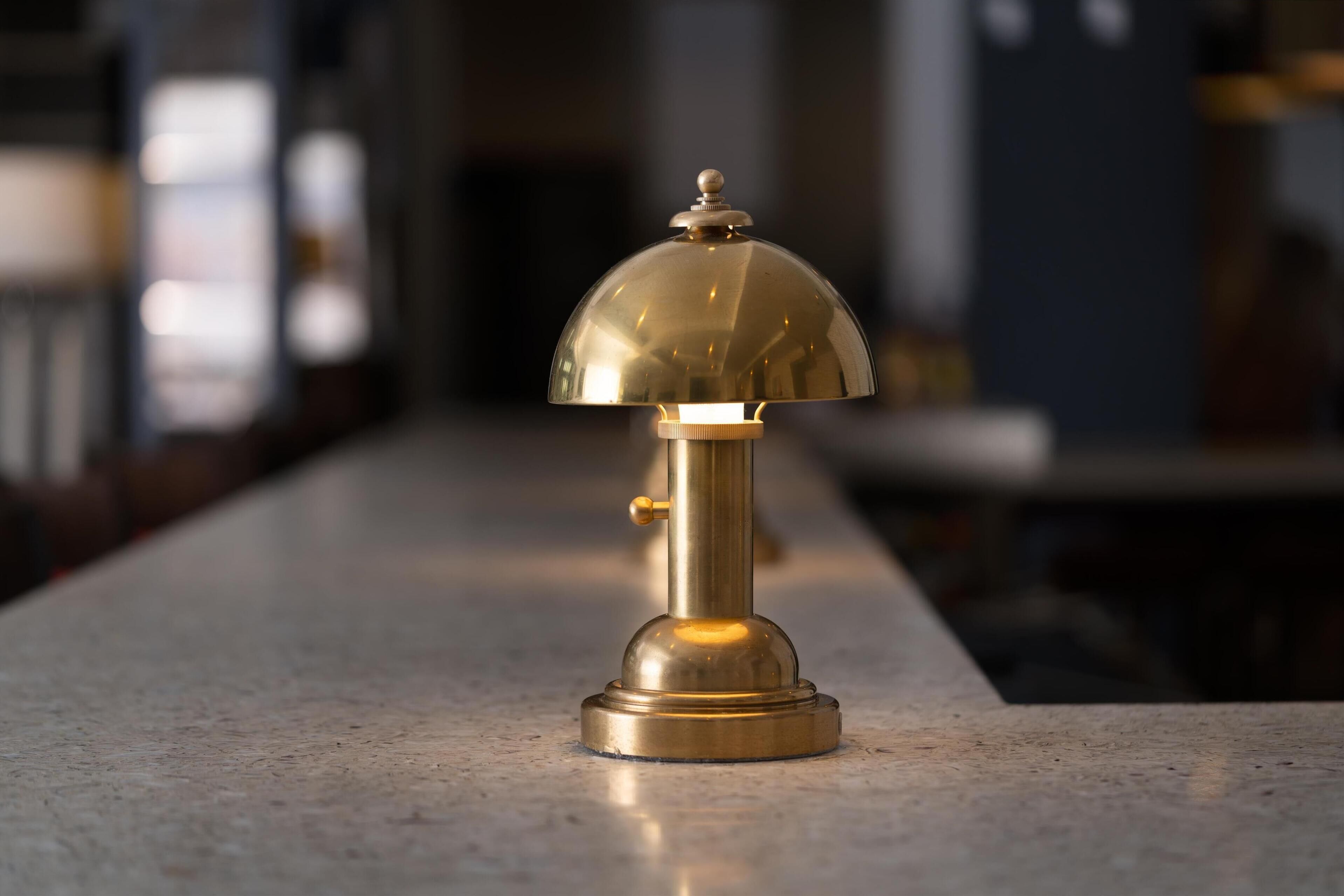 A brass table lamp with a dome shade on a marble countertop.