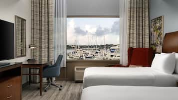 A hotel room with a large window offering a marina view, a desk with a chair, a bed, and a TV.