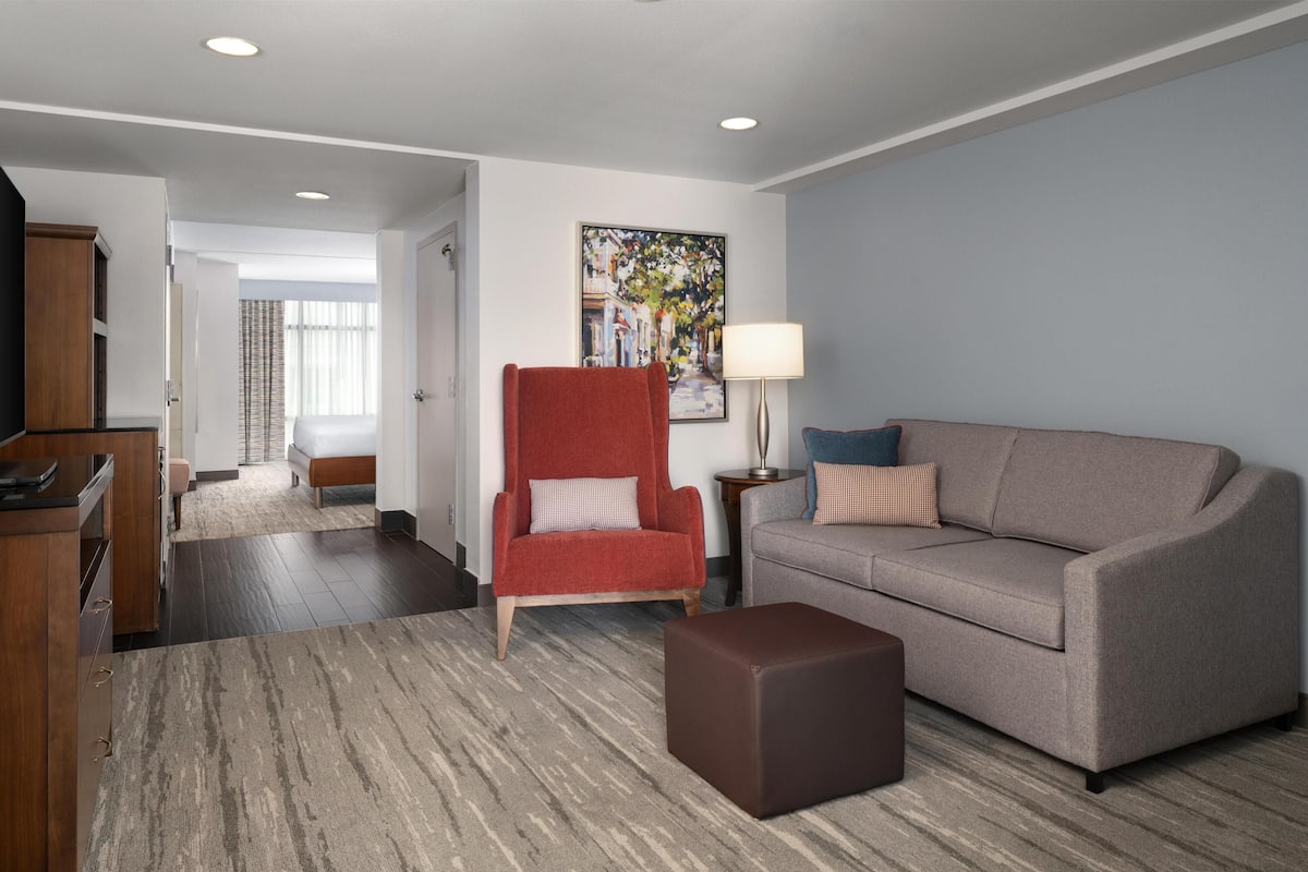 A modern living room with a sofa, armchair, ottoman, and a painting on the wall.