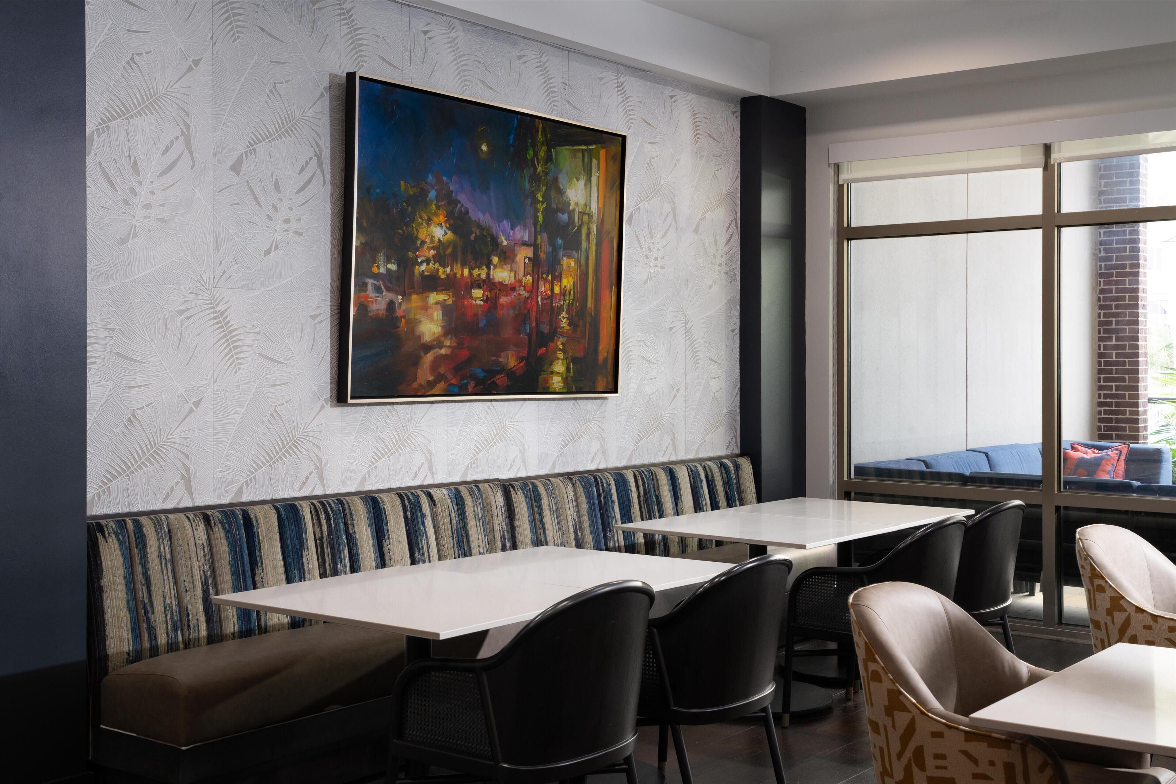 Ein Restaurant mit einem großen Gemälde an der Wand, einer gemusterten Wand und Blick ins Freie durch große Fenster.