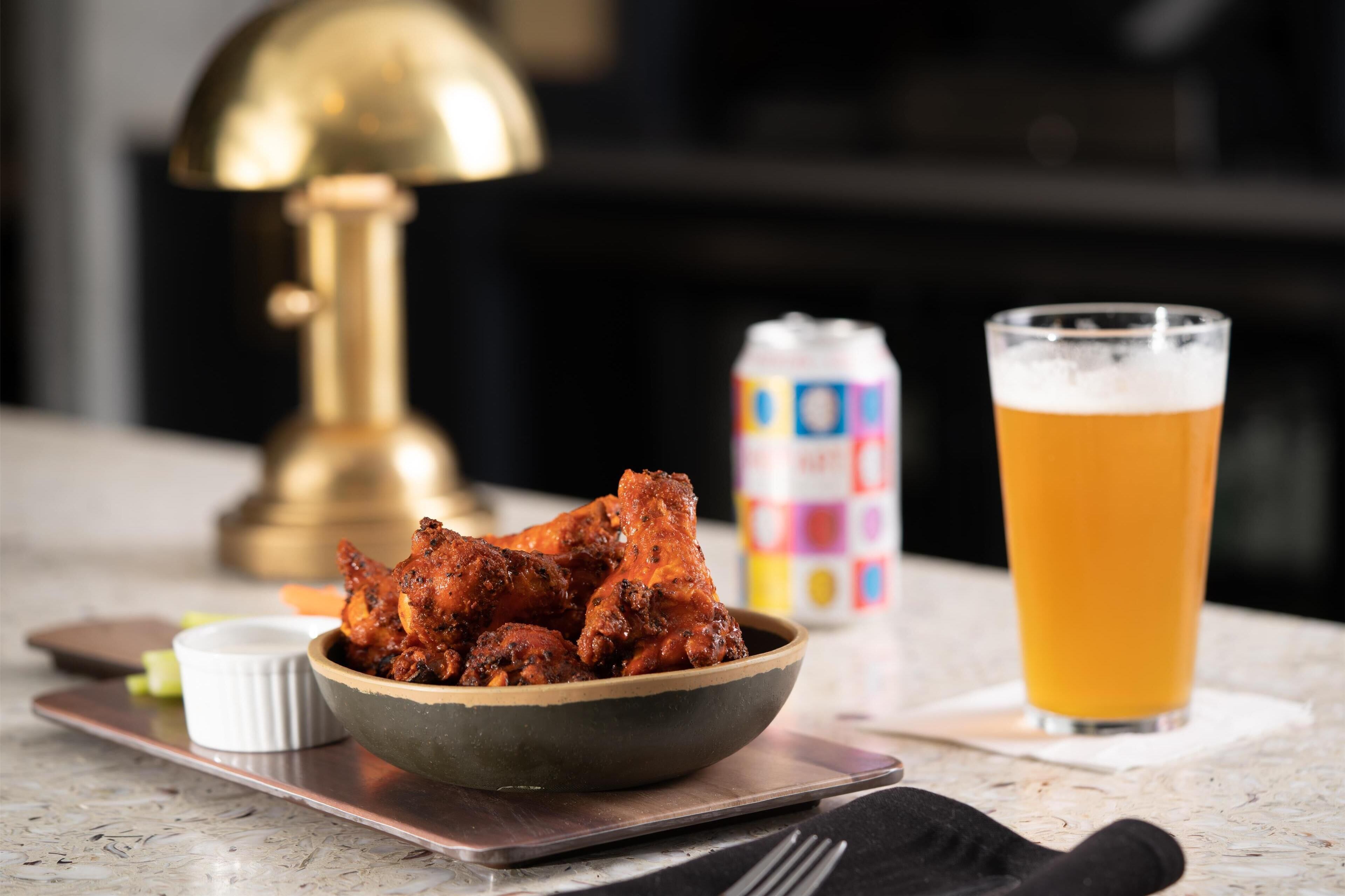 Une table avec un bol d’ailes de poulet, une canette de soda et un verre de bière.