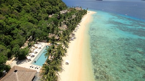 A beach resort with a swimming pool, lounge chairs, and a view of the ocean and mountains.