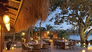 An outdoor dining area with tables and chairs, a pool, and a view of the sea.