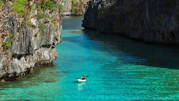 A kayaker in a clear turquoise river surrounded by rocky cliffs.