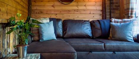 Interior acogedor de una cabaña con pared de madera, un espejo redondo, un sofá de cuero y una pequeña mesa con una planta.