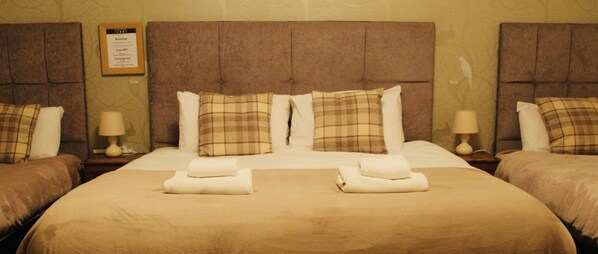 A hotel room with two beds, each with a brown headboard, white bedding, and plaid pillows. There are two bedside tables with lamps.