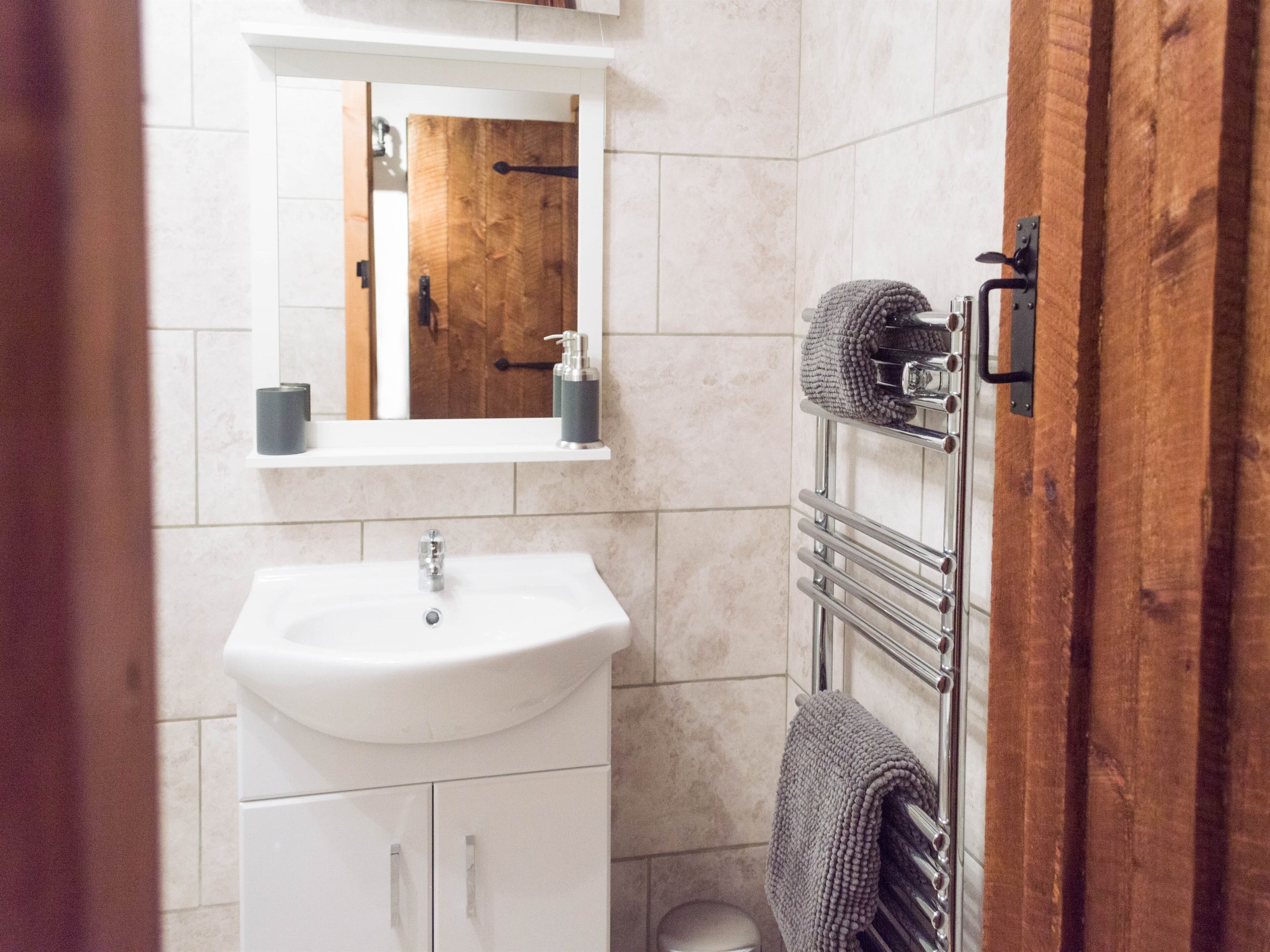 A bathroom with a white sink, a mirror, a wooden door, and a towel rack.