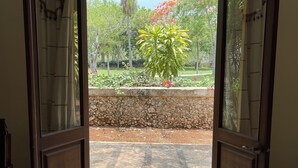 Una puerta abierta que da a un jardín con pared de piedra, una planta en maceta y vistas a árboles y flores.