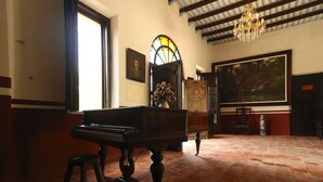 Un piano de cola en una habitación amplia con suelo de baldosas, una araña y un cuadro grande en la pared.