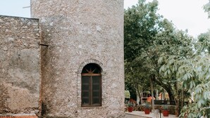 Una torre de piedra con una ventana, rodeada por un jardín con plantas en macetas y un sendero.