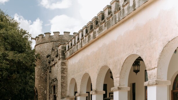 Un patio con suelo de piedra, columnas blancas y un edificio de piedra con arcos.