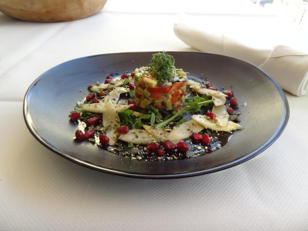 A plate of food with a central mound of ingredients, surrounded by various vegetables and garnishes.