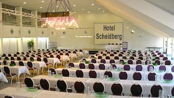 A large banquet hall with rows of tables and chairs, a chandelier, and a sign reading "Hotel Scheidberg".
