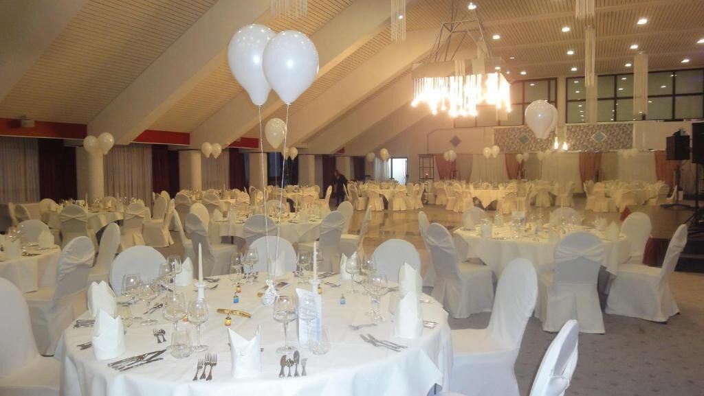 Une salle de banquet avec des tables rondes dressées pour un événement formel, des nappes blanches et des chaises recouvertes de housses blanches.