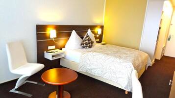 A hotel room with a bed, bedside table, chair, and a small round table.