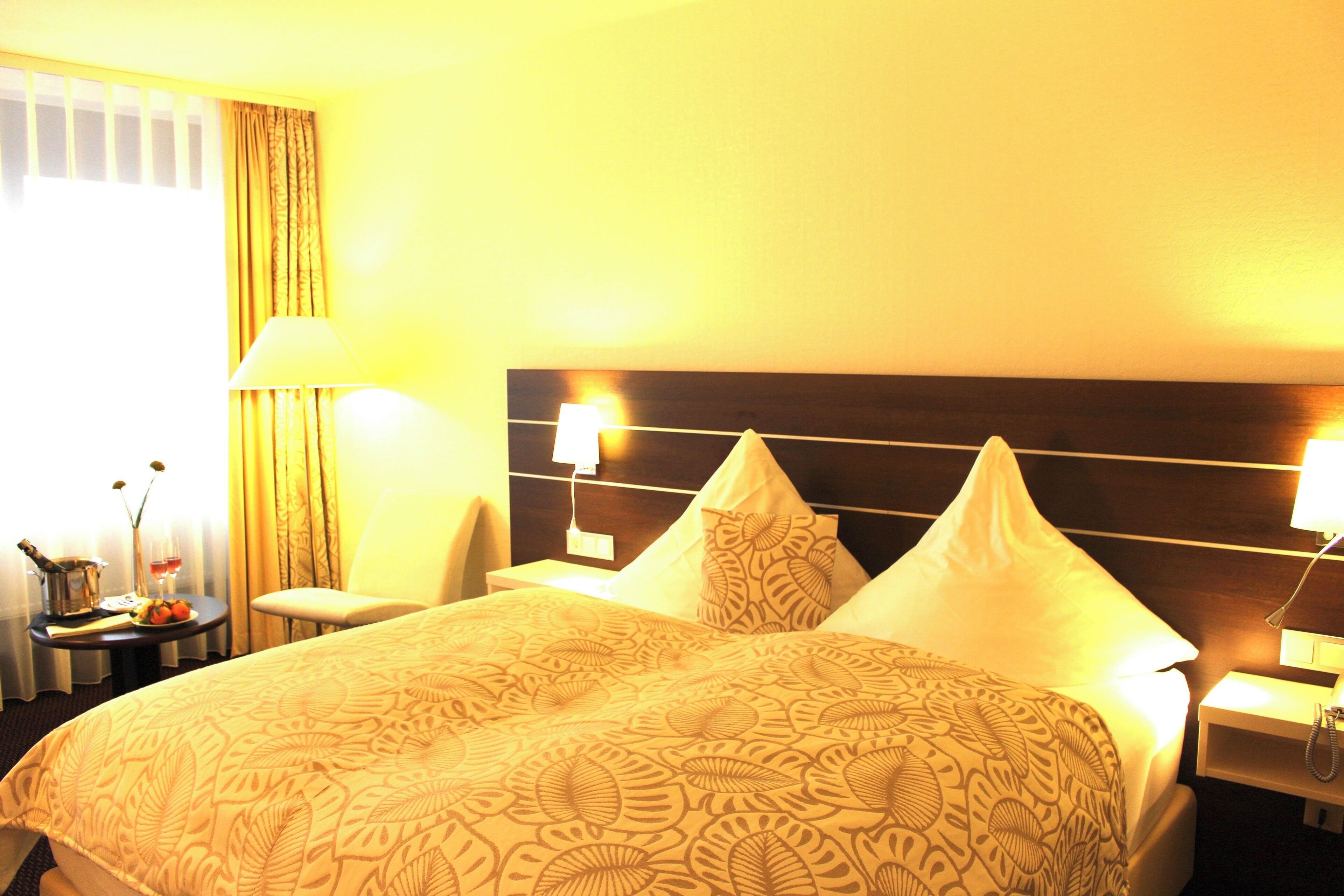 A hotel room with a large bed, two bedside lamps, a nightstand with a phone, and a window with curtains.