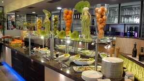 A buffet counter with various food items and a display of decorative fruit sculptures. - Hotel Scheidberg (Wallerfangen)