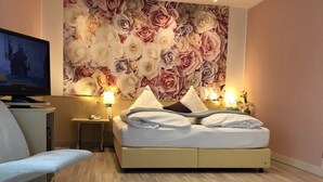 A hotel room with a bed, a desk, a chair, a television, and a floral wall mural. - Hotel Scheidberg (Wallerfangen)