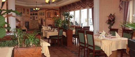 A restaurant with multiple tables, chairs, and potted plants.