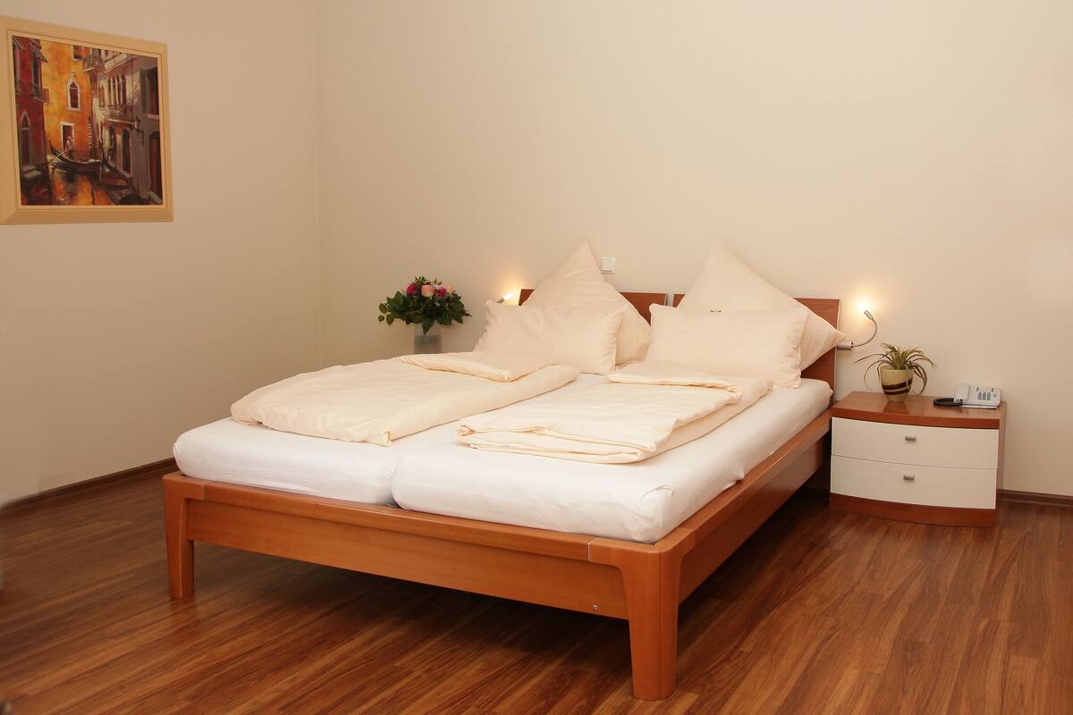 A neatly made double bed with a wooden frame, a bedside table with a lamp, and a small potted plant.