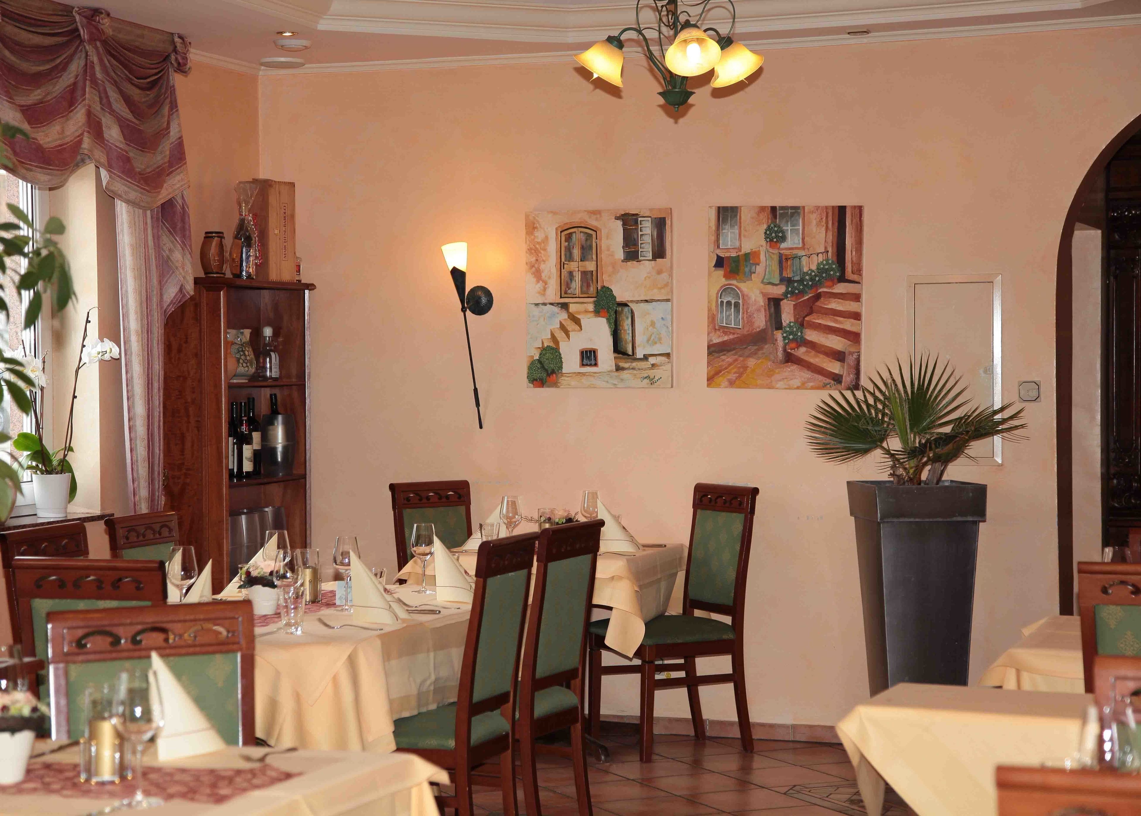 A dining area with tables set for a meal, chairs, a chandelier, and wall art.