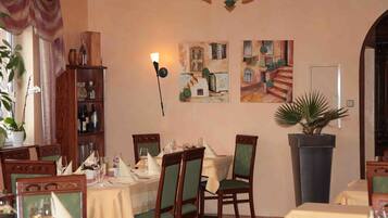 A dining area with tables set for a meal, chairs, a chandelier, and wall art.