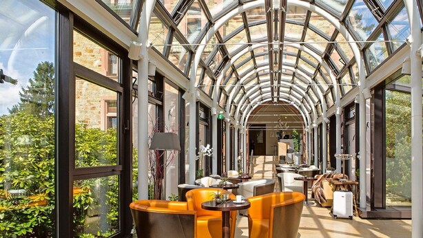 A glass-enclosed corridor with seating areas and a view of the outside. - Romantik Hotel Schloss Rettershof (Kelkheim)
