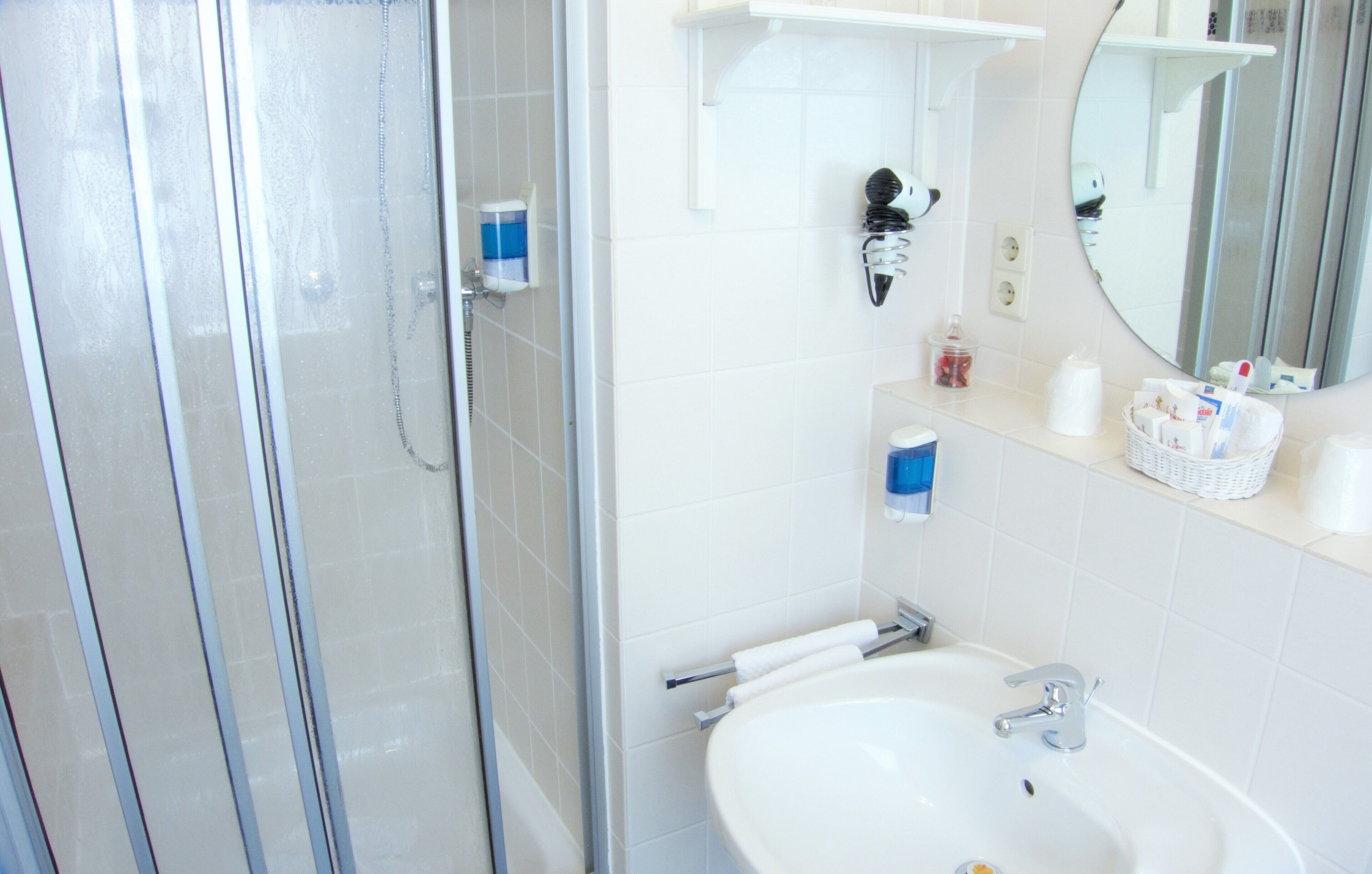 A bathroom with a glass shower enclosure, a sink with a mirror, and toiletries on the countertop.
