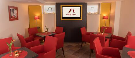A hotel lobby with red chairs and tables, a large screen displaying the hotel name, and a modern design.