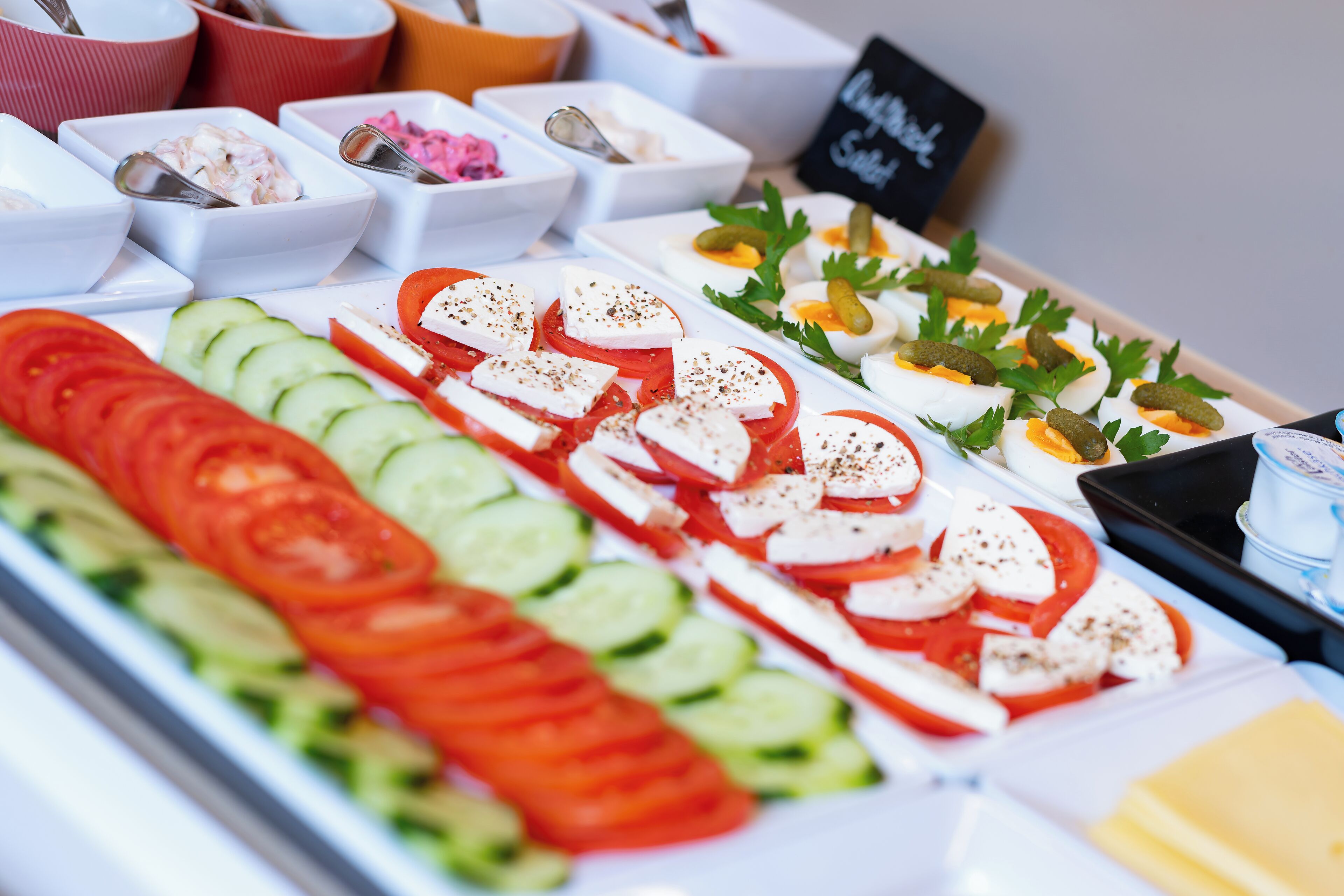 A buffet with various food items including sliced tomatoes, cucumbers, mozzarella cheese, and garnishes.
