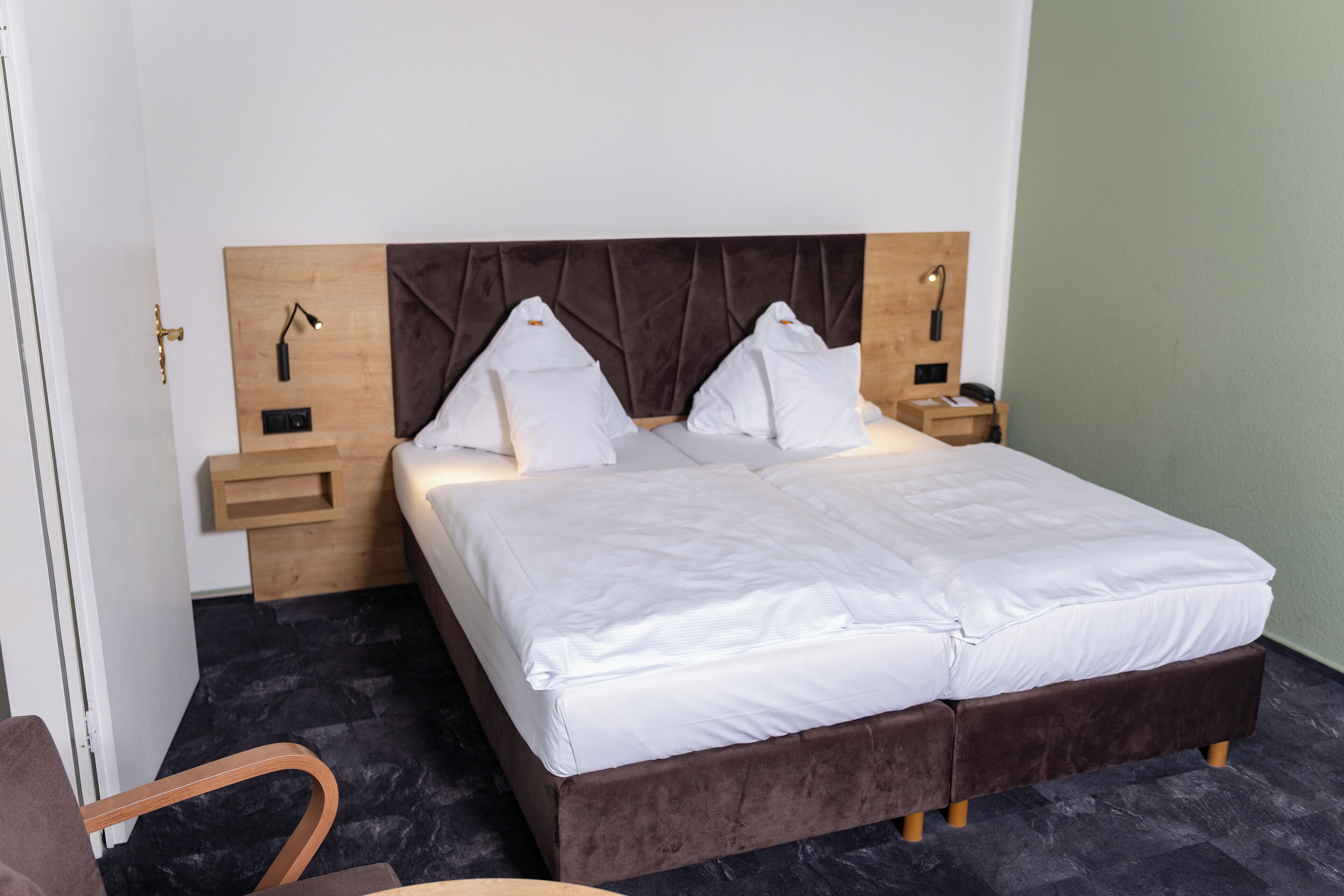 A neatly made bed with white linens, a wooden headboard, and two bedside tables with lamps.