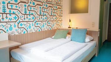 A neatly made bed with white linens and two pillows, a bedside table with a lamp, and a patterned wall.