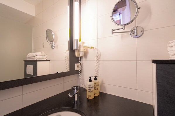 A bathroom with a black countertop, a sink, a mirror, and two bottles of shampoo. - Hotel Madeleine Saarbrücken City (Saarbrücken)