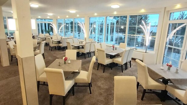 Ein geräumiges Restaurant mit mehreren Tischen und Stühlen, großen Fenstern und einem Teppichboden.