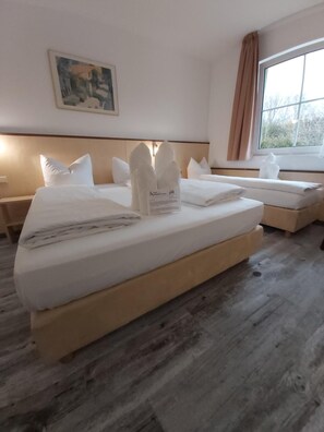 Una habitación de hotel con cama, mesita de noche, ventana con cortinas y un cuadro en la pared.