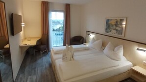 Ein Hotelzimmer mit zwei Betten, einem Schreibtisch, einem Sessel, einem Fernseher und einem Bild an der Wand.