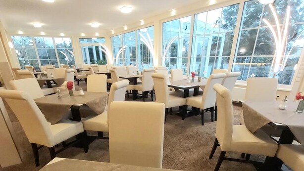 Ein Restaurant mit mehreren Tischen und Stühlen, großen Fenstern und Blick auf Bäume.