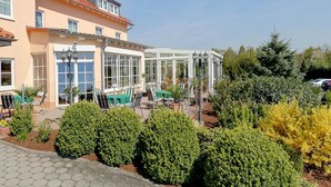 Ein Gebäude mit überdachter Außenbereich, Wintergarten und Garten mit ordentlich geschnittenen Büschen.