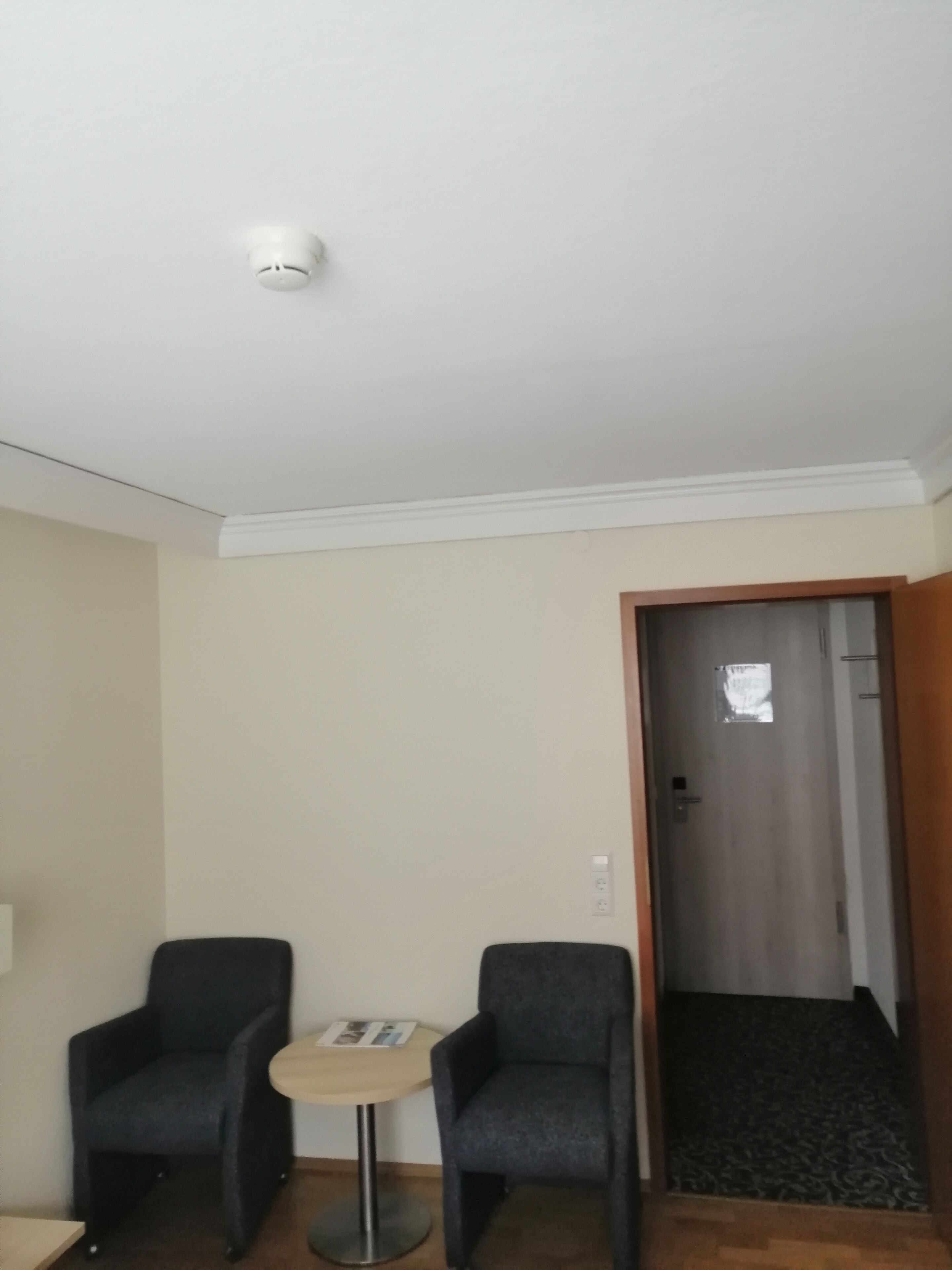 Habitación de hotel con dos sillones, una mesita redonda, una lámpara del techo y una puerta que da a una escalera.