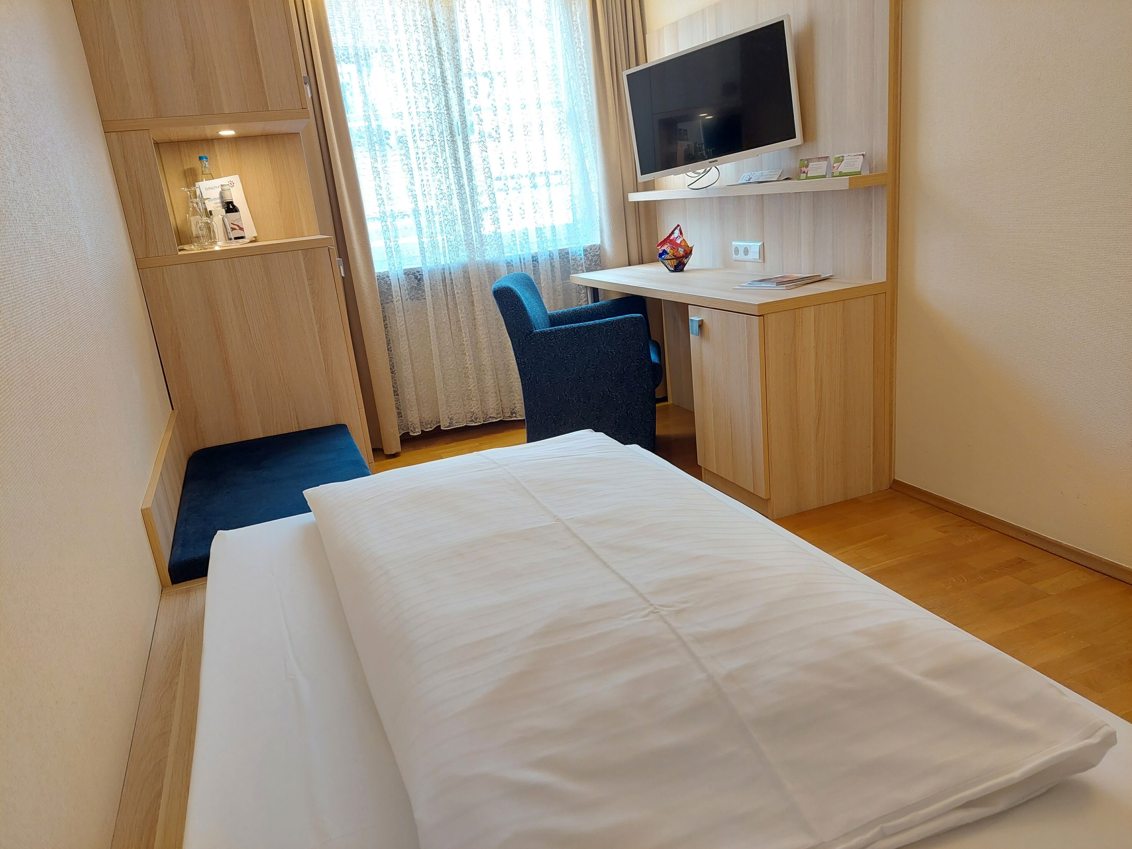 Una habitación de hotel con cama, escritorio, silla, televisión y ventana con cortinas.
