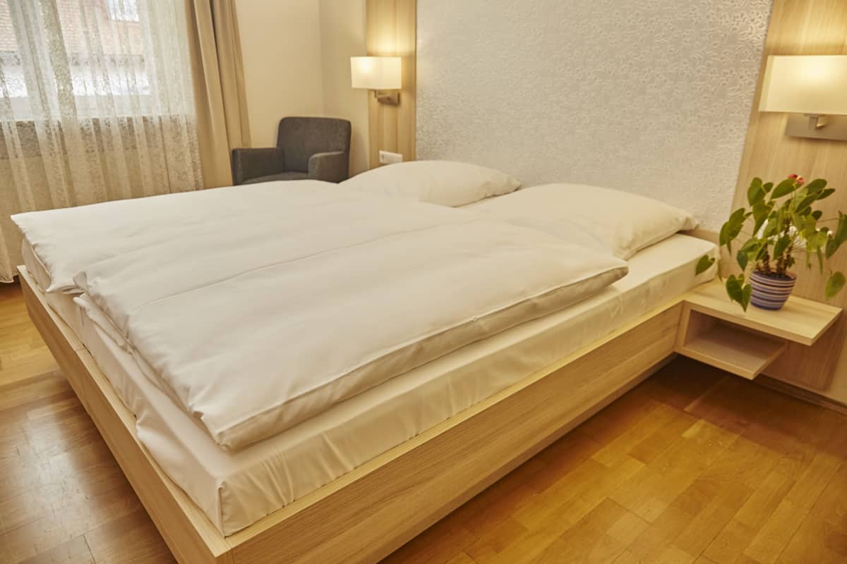 Een tweepersoonsbed met houten frame, een nachtkastje met lamp, een stoel en een kamerplant.