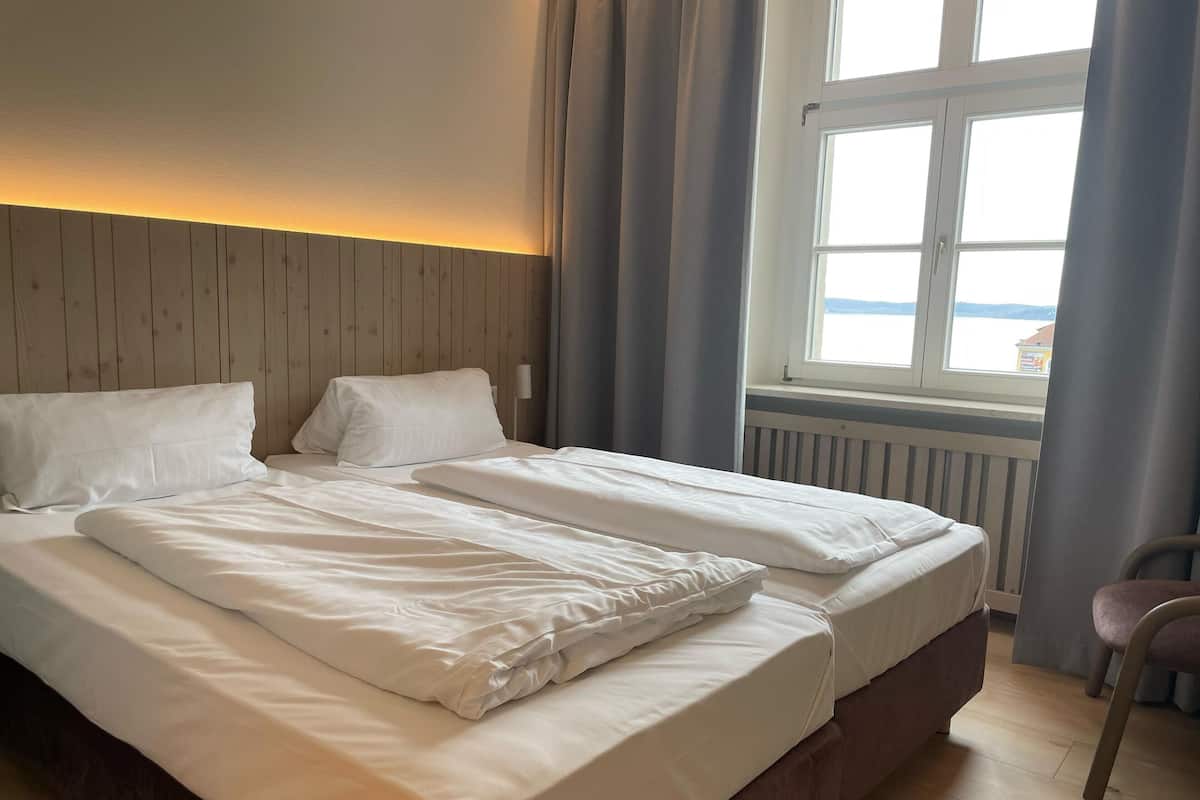 Een tweepersoonsbed met witte lakens in een kamer met houten lambrisering en een raam met gordijnen.