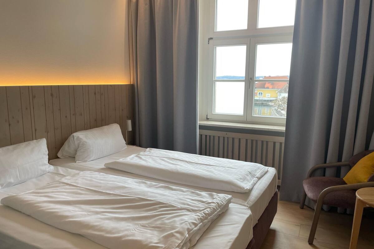Een hotelkamer met twee bedden, uitzicht op de stad door een raam en een stoel bij het raam.