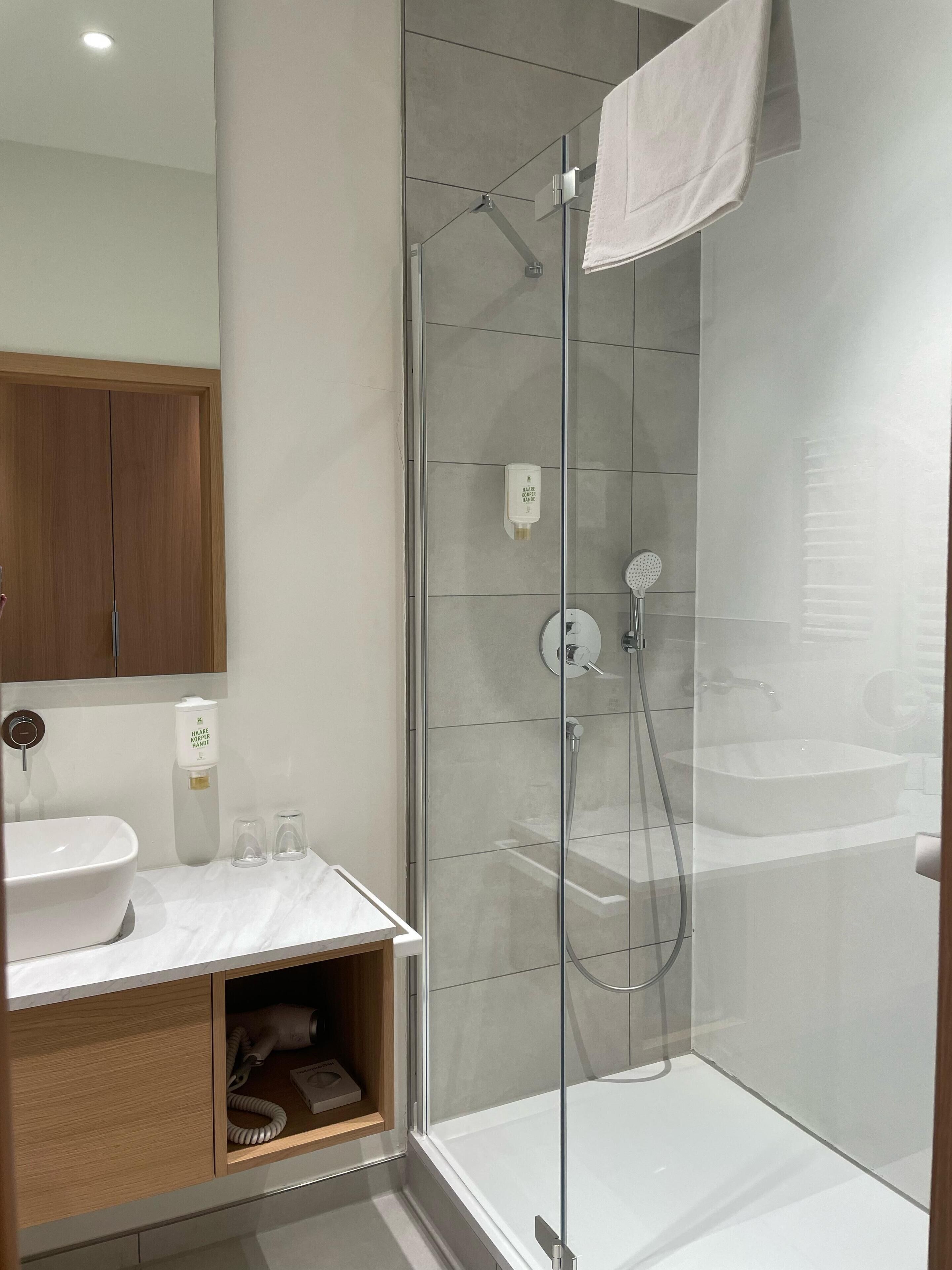 Une salle de bain moderne avec une douche à parois de verre, un lavabo blanc et un meuble-lavabo en bois.