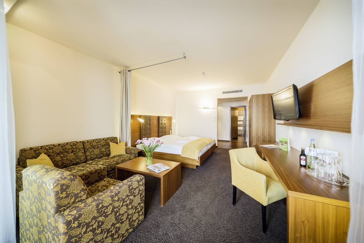 Een hotelkamer met een bank, een bed, een bureau met televisie en een kleine tafel met een bloemenvaas.