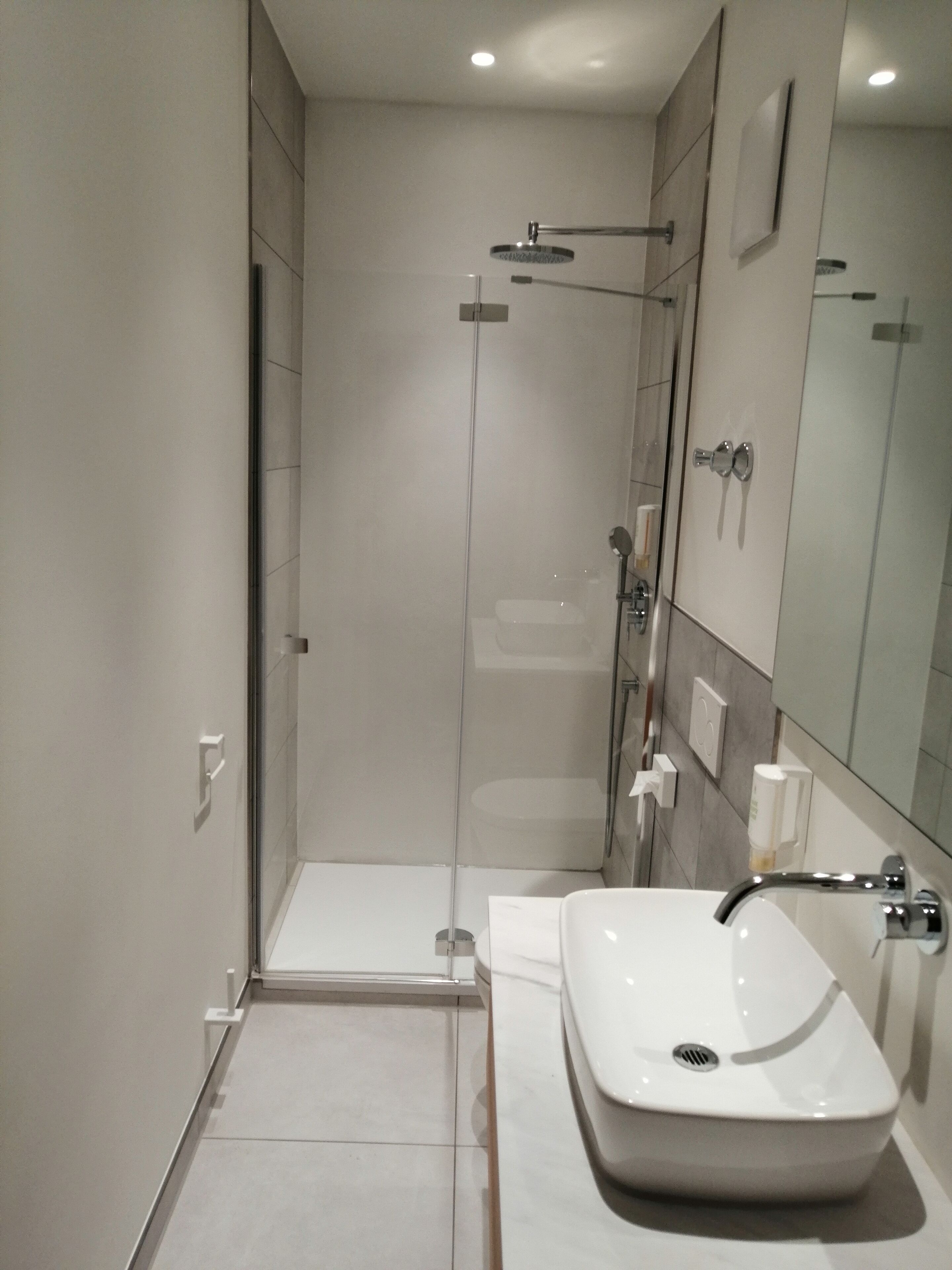 Ein modernes Badezimmer mit einer gläsernen Dusche, einem weißen Waschbecken und einem großen Spiegel.